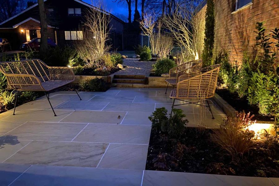 Seen at night, the beige smooth sandstone paving slabs show veining and it's flat surface next to soft up lights.