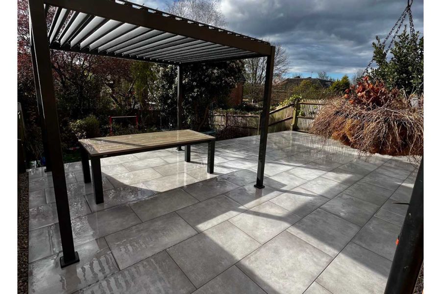 Raised Venetian Grey Porcelain patio area with metal pergola and dining table with over cast skies.