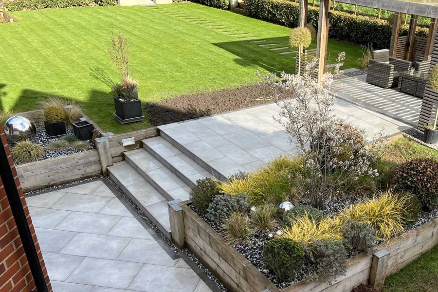 Multi level Venetian Grey Porcelain Patio with matching steps and surrounded by raised timber sleeper planted flower beds.