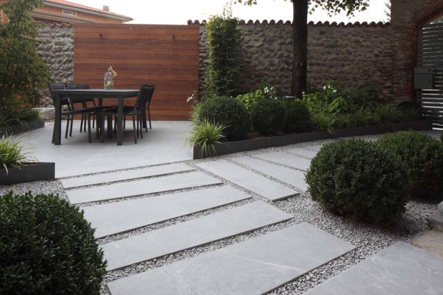 Tall stone walls enclose garden paved in Versilia outdoor tiles. Bespoke trapezium-shaped tiles laid in gravel in foreground.