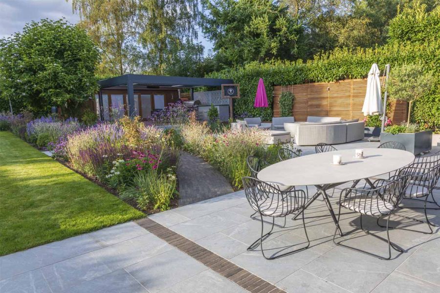 Outdoor furniture on Versilia Porcelain patio. Clay paver path leads to pergola between flower beds. By Chiltern Garden Design.