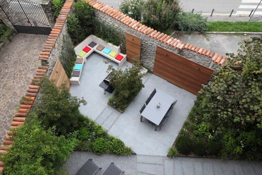 Aerial view of Versilia Vitrified Porcelain patio. Gas barbecue and dining set are separated by a bed thickly planted with shrubs.