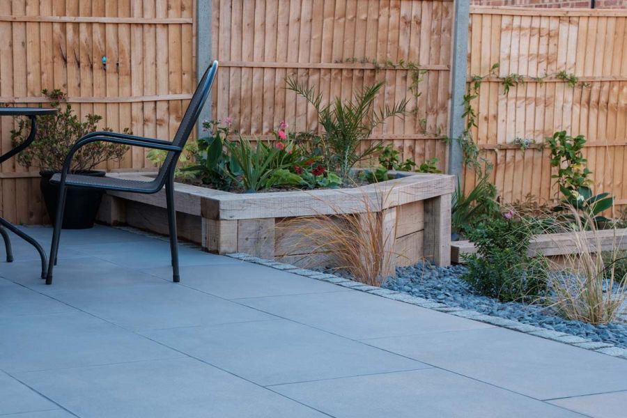 Raised porcelain patio with a closed board fence behind and timber raised flower beds set at different levels.