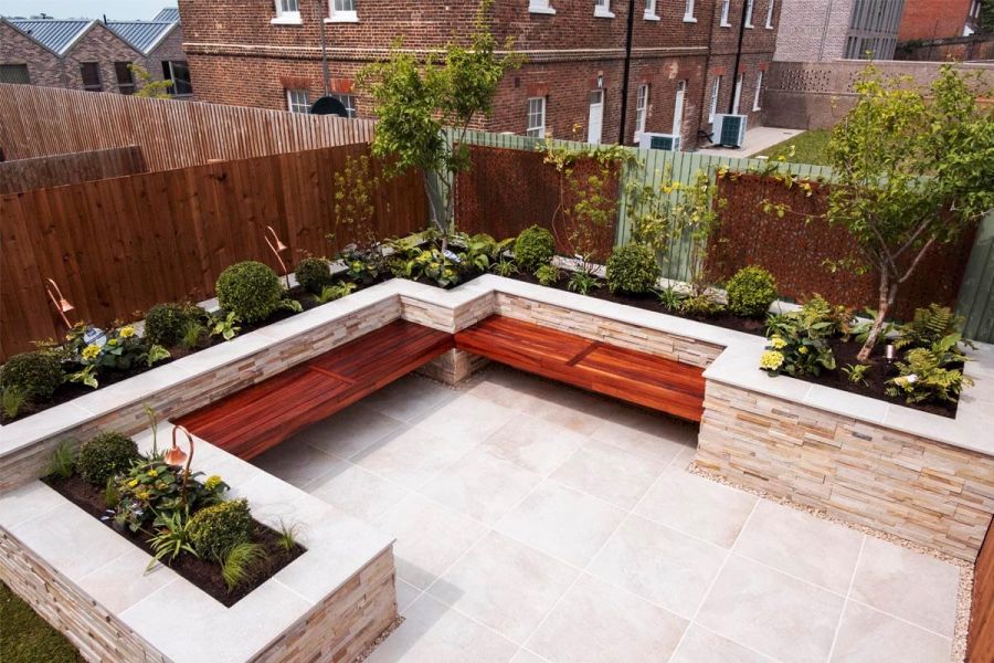 Small back garden area paved with Gea porcelain tiles featuring a seating area cladded with mint sandstone exterior cladding.