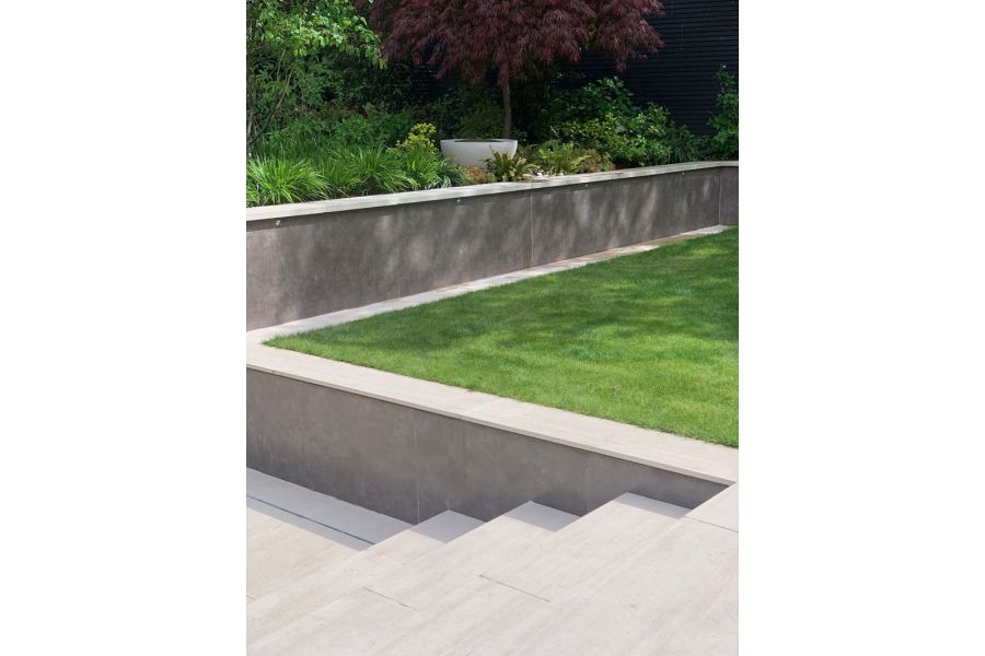 Steps descend from level of lawn to path next to retaining wall faced with Vulcano Ceniza luxury DesignClad wall cladding. 