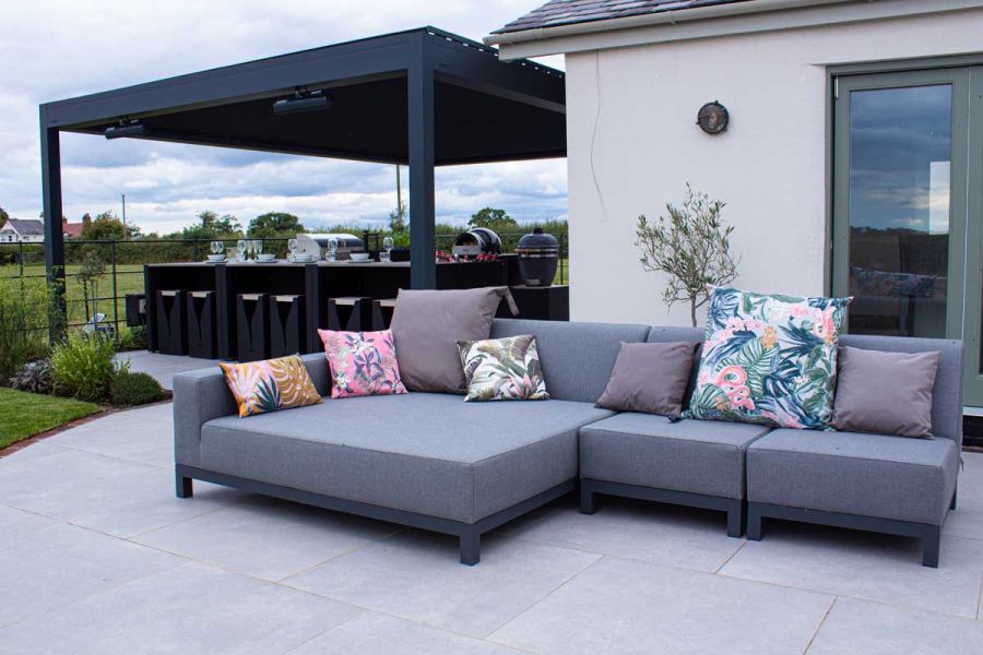 Polvere porcelain Large Paving Slabs paved under a large black pergola with BBQ and dining area and relaxing outdoor furniture.