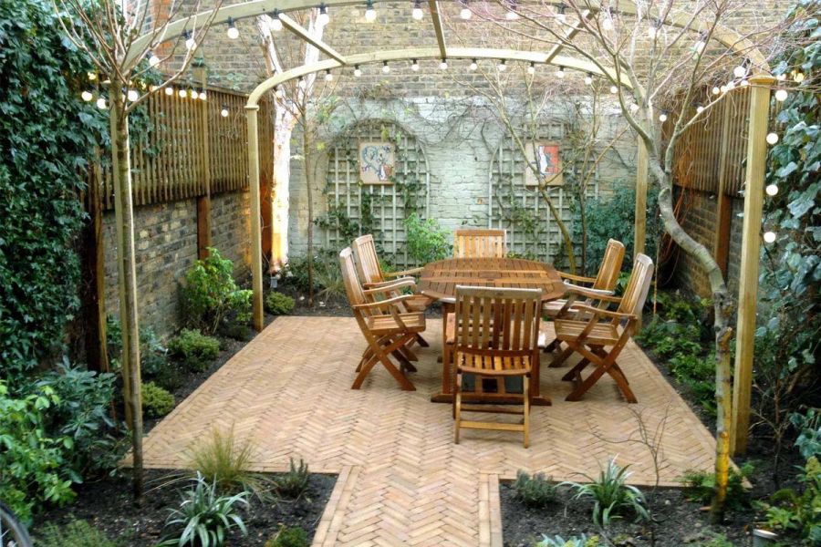 Pergola over wooden dining set on Westminster Clay Pavers in small walled back garden. Design by Mark Wallinger Landscapes.