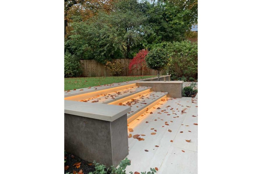 3 wide steps of Faro porcelain paving scattered with fallen leaves rise to lawn from matching paving. Design by Waratah Gardens.