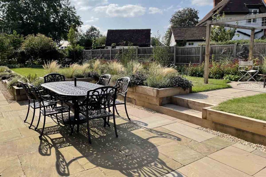Dining set on Raj Green Indian sandstone patio with raised lawn behind retained by timber sleepers. Design by Wilson Associates.