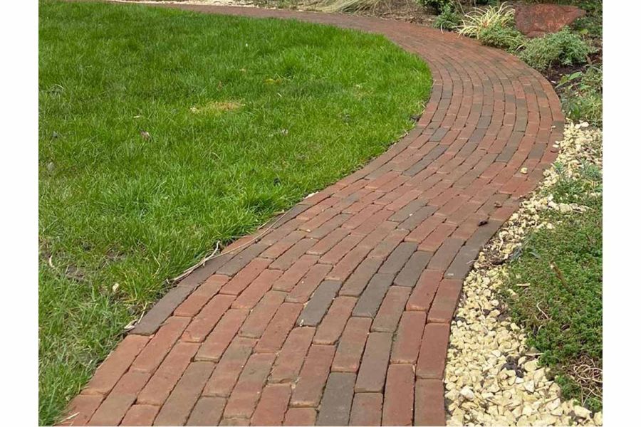 Close view of grey, red and brown Winton Brick pavers laid running bond in curved path next to lawn by Landscape Artisan.