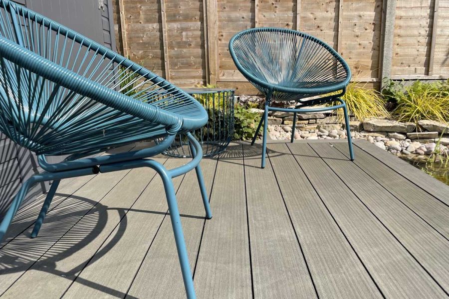 2 wire chairs sits on raised deck of Charcoal composite decking boards, next to gravel bed with grasses. Design by Martyn Wilson.