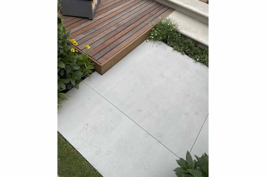 Large Yard porcelain patio slabs laid tight up against a raised timber deck with small planting pockets set around the paving.