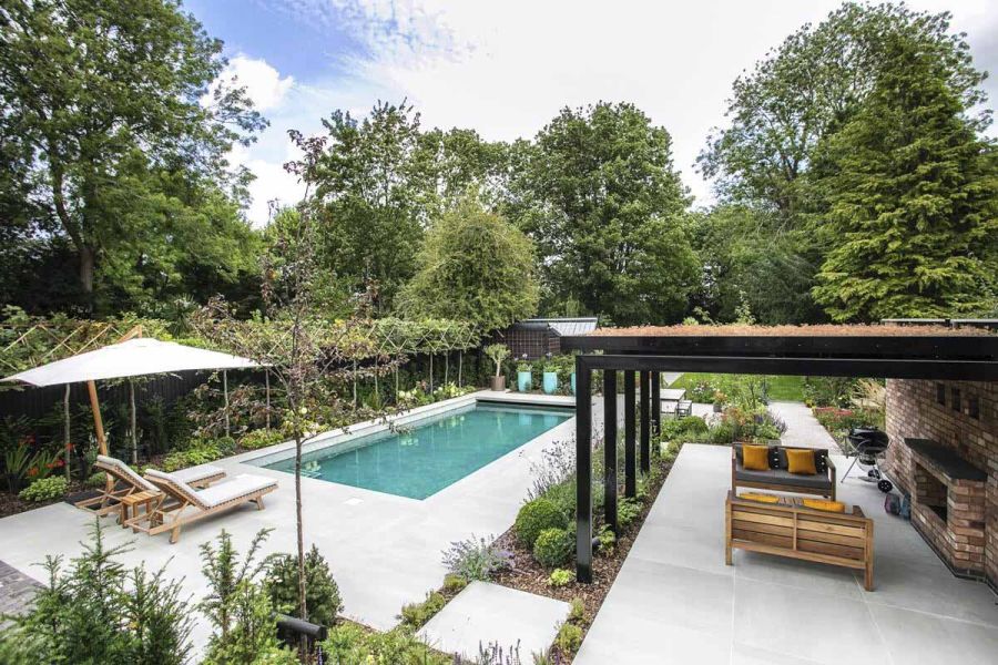 Large garden surrounded by trees, paved in Yard Outdoor Porcelain Paving, with pergola, swimming pool and garden furniture.