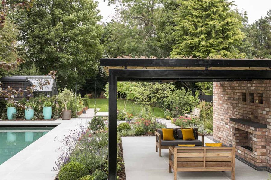 Pergola mounted on wall with built-in barbecue covers seating area paved in Yard 1200 X 1200 Porcelain tiles, with lawn beyond.