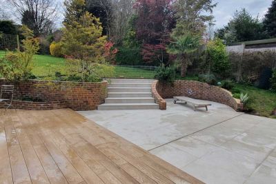 Decking area next to Area 800x800 Porcelain Paving, integrated steps leading up to a lawn, and large paving slabs adjacent to a red brick wall.***Garden House Design, www.gardenhousedesign.co.uk