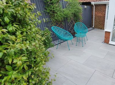 Kandla Grey Porcelain paving, with turquoise wire chairs and table against fence with trellis, designed by Absolute Landscapes.***Absolute Landscapes Ltd,  www.absolutelandscapesltd.co.uk