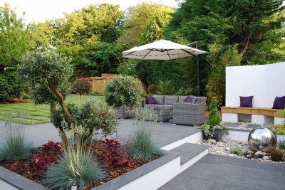 L-shaped patio of Black granite paving with cloud-pruned tree in raised bed opposite rattan sofa and free-standing parasol.***The Landscape Design Studio, www.thelandscapedesignstudio.co.uk