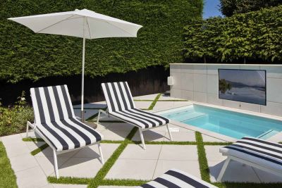 Outdoor TV wall above swimming pool, sun-loungers and parasol nearby, with surrounding area paved with Comblanchien patio tiles.***PWP Landscape,  www.pwplandscape.co.uk