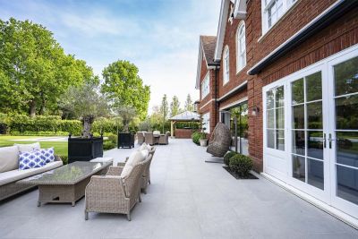 Florence Grey outdoor tiles UK stretch across width of house, with 2 sets of rattan furniture, olive tree planters and topiary.***Elitescapes, www.elitescapes.co.uk
