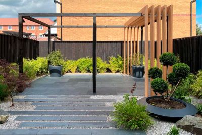 Dark-fenced garden paved with Brazilian Grey stone slabs  and planks set in gravel, with cloud-pruned shrub in shallow pot.***Designed by Robert Hughes Studio, www.roberthughesgardendesign.co.uk | Built by Outside Edge Landscapes, www.oelandscapes.co.uk