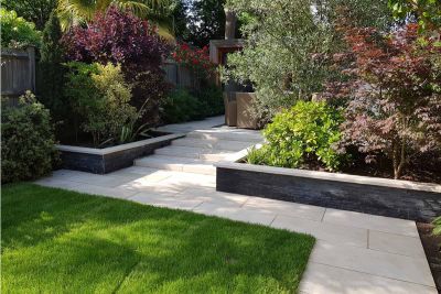 In mature garden, path of Slab Khaki Porcelain Outdoor Tiles UK leads to steps, with flanking wall topped with matching coping.***John Gale Landscapes,  www.johngale-landscapes.co.uk
