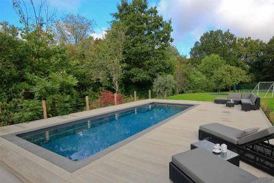 Sun loungers on Smoked Oak Millboard decking surround of swimming pool with stone coping edges, in lawned garden bordered by trees.***Designed by Karen McClure Garden Design, www.karenmcclure.co.uk | Built by Langdale Landscapes, www.langdalelandscapes.co