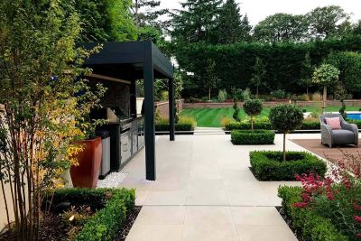 Golden Stone Porcelain patio with outdoor kitchen, metal pergola and decking set flush to paving, by The Landscape Design Studio.***The Landscape Design Studio, www.thelandscapedesignstudio.co.uk
