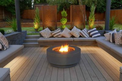 Firepit burns in centre of sunken seating area lined with benches, laid with Traditional WPC decking, designed by Landscapia***Landscapia Garden Design & Build,  www.landscapia.co.uk