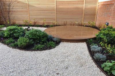 Round raised Millboard decking finished with flexible bullnose edging in corner of gravel-paved garden with curve-edged beds.***Urban Landscape Design Ltd, www.urbanlandscapedesign.co.uk