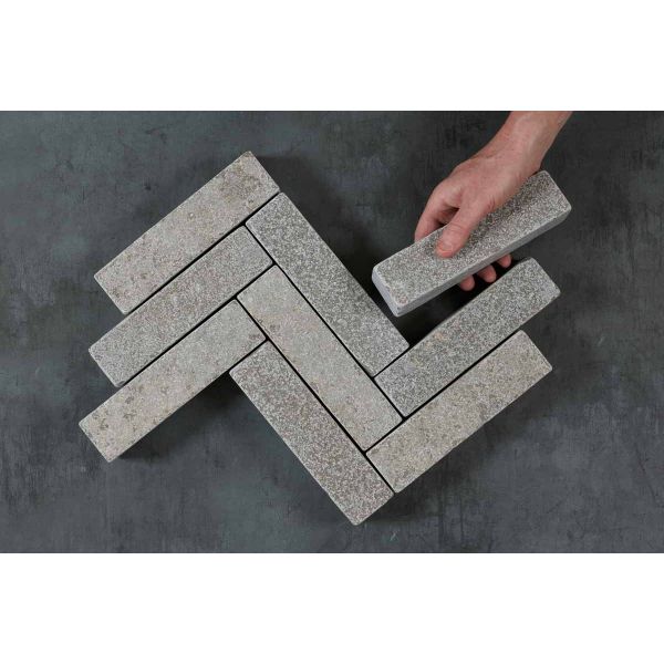 Hand places one Antique Grey limestone brick paver against 9 laid in 3 zigzag rows on dark background. Free UK delivery available.***