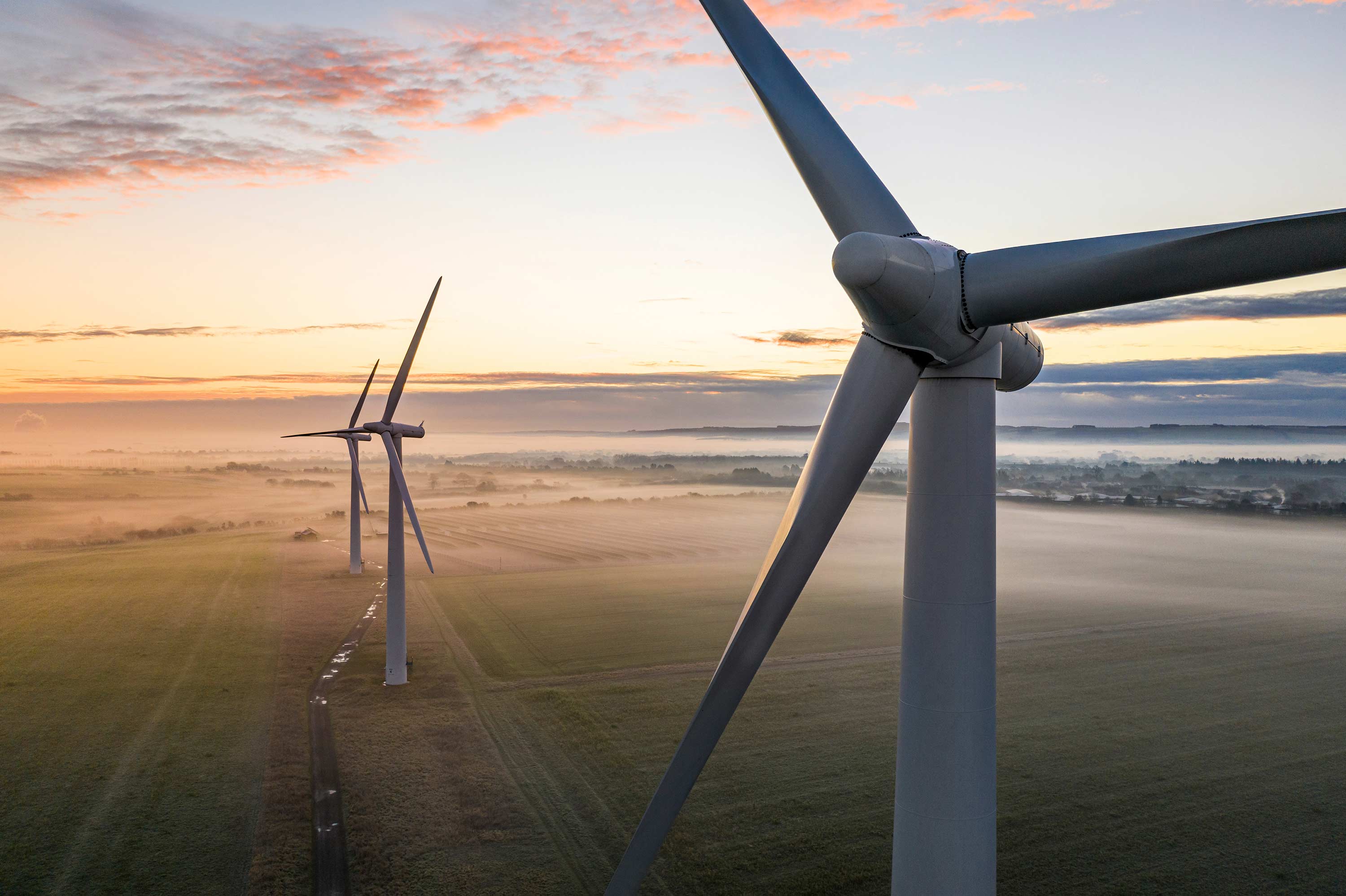 Panning shot of wind turbines from level of blades, looking out to countryside.