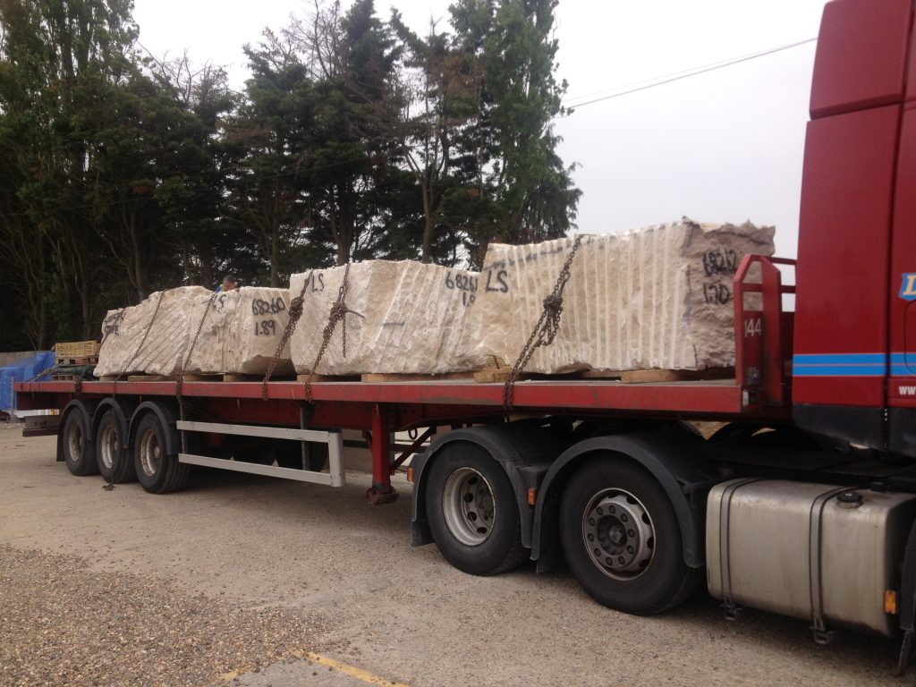 Large articulated truck carrying blocks of stone covered in tarpaulins.