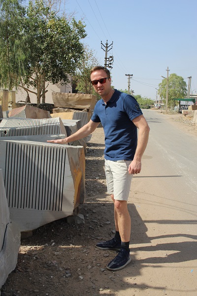 Man standing next to block of sandstone with calibrated slabs still attached. 