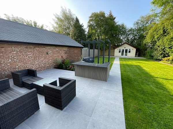 Large Faro porcelain patio by side of low brick building with outdoor kitchen and long path to garden shed.