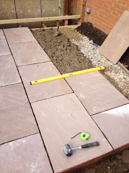 Part finished sandstone patio with mortar bed, spirit level, tape measure and string lines