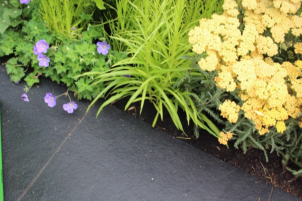 Black limestone treated with colour enhancing sealer with rich green leaves and yellow flowers spilling over the edge.