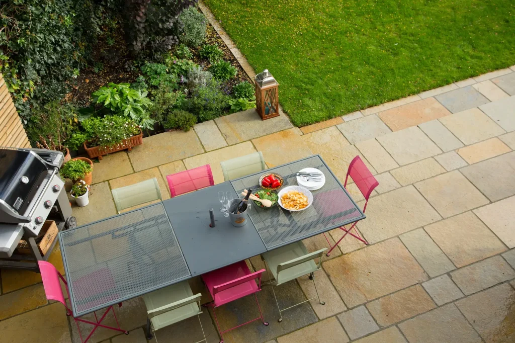 View down onto Antique Yellow limestone patio with dining table and barbecue next to planted bed and lawn
