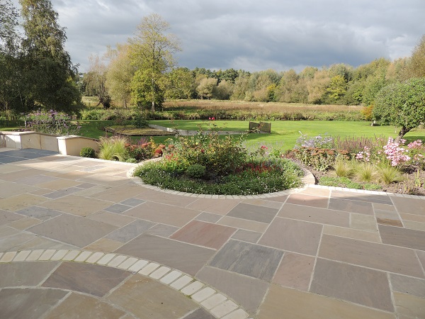 Raj Green sandstone patio with round inset bed looks out over large lawn to distant trees. 