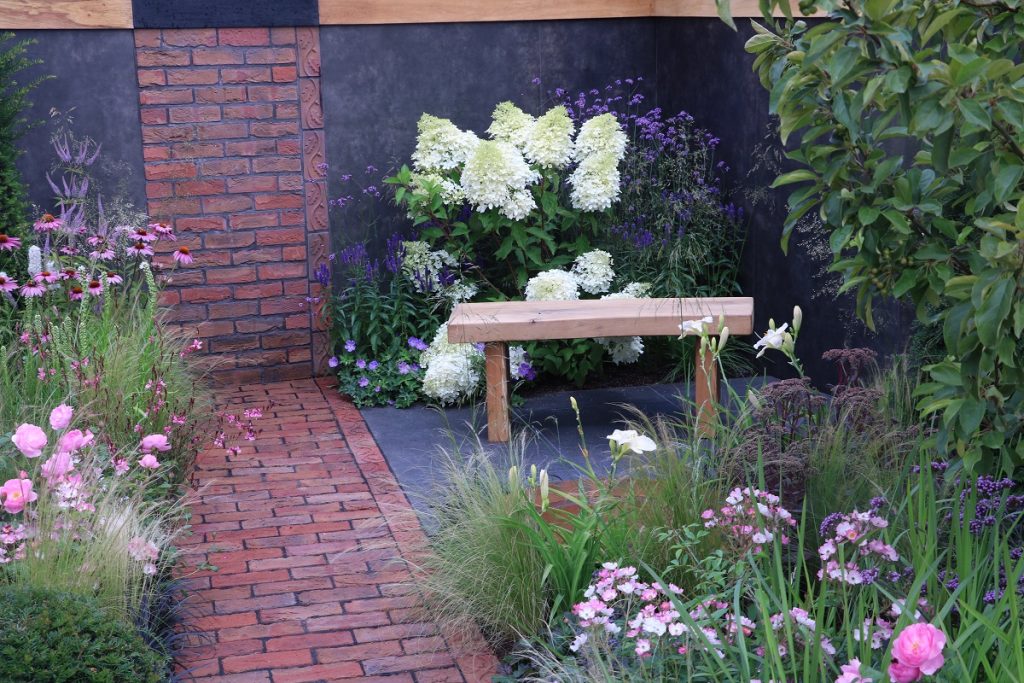 Garden paving ideas from Matt Haddon, combining black granite paving and clay pavers with bench and DesignClad Volcano Roco clad walls.