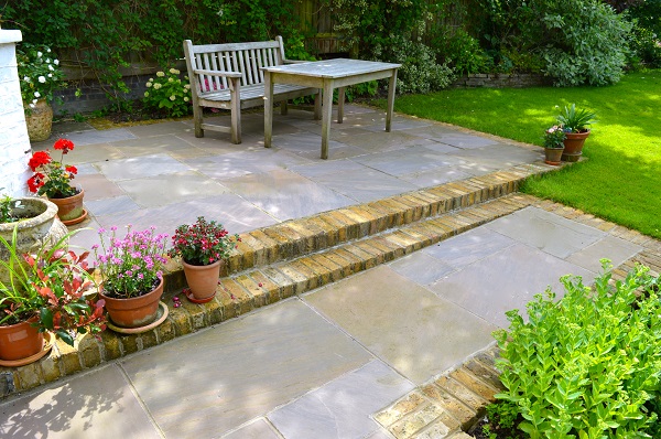 2 brick steps up to patio of Autumn Brown riven sandstone with bench and table. Design by Steve Hooper Landscapes