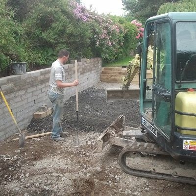 Man with rake and digger spread deep MOT Type 1 sub base during paving installation