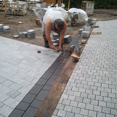 Experienced landscaper bending to lay setts. 