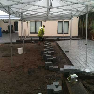 Man doing paving installation of silver grey granite setts under a gazebo.