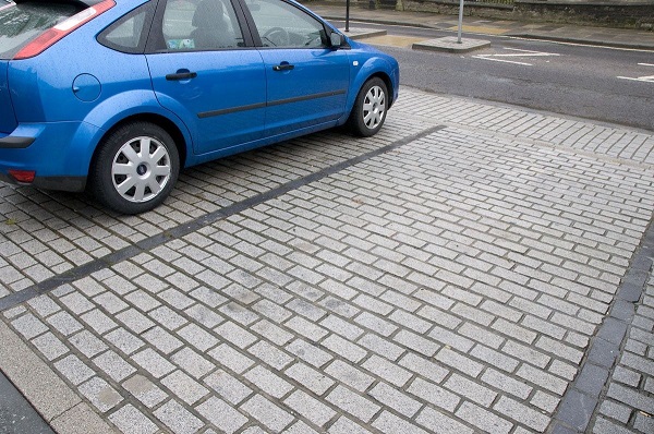 Blue car on one half of driveways of granite setts with GftK grouting. Pavement and road beyond. 