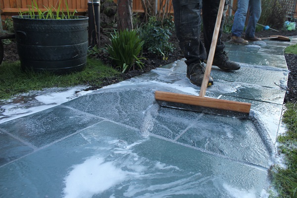 Bottom of legs of person pointing a riven stone pathway with brush-in jointing compound.