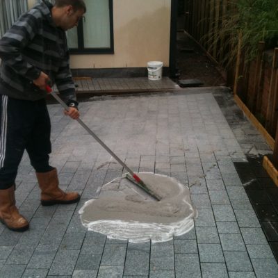 Man with rubber squeegee spreading sweep-in jointing compound during paving installation