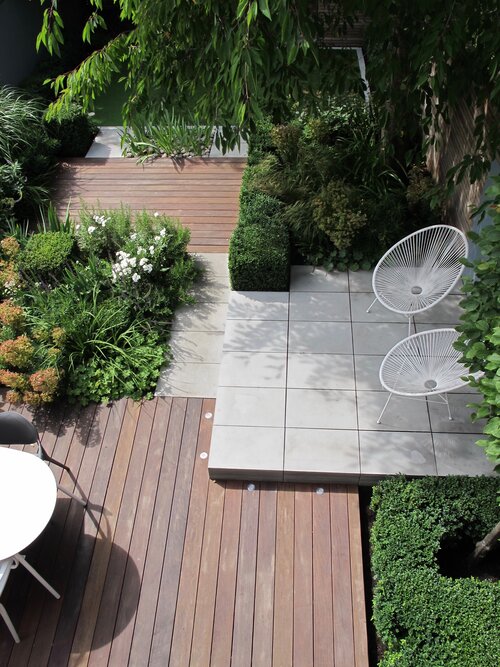 View down onto small patio in Contemporary Grey sawn sandstone, decking and bushes. Design by Lucy Willcox