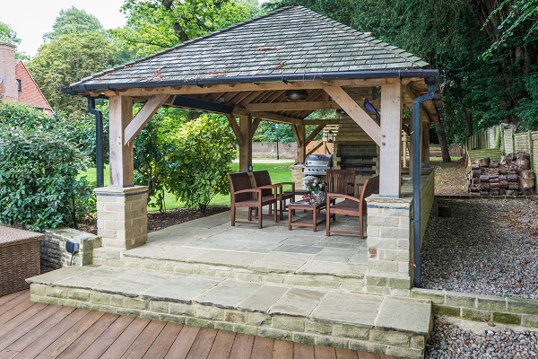 Roofed square  pergola with a raised floor of reclaimed Yorkstone, trees behind. 
