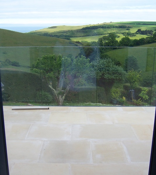 View across sandstone patio with mortar stains to Devon valley seen through glass railings.