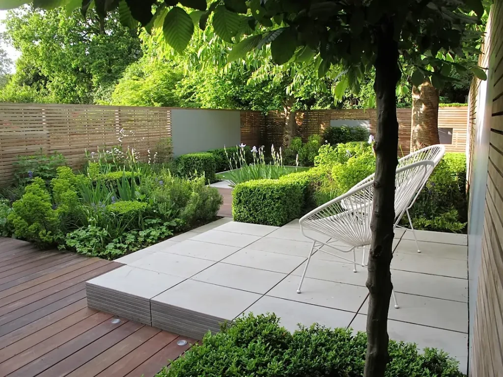 Garden with clipped hedges, raised Contemporary Grey sandstone patio and decking.